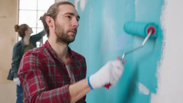 Couple caucasien à la maison ensemble peinture murs gros plan à la caméra homme peinture murs avec le rouleau de brosse murale — Video