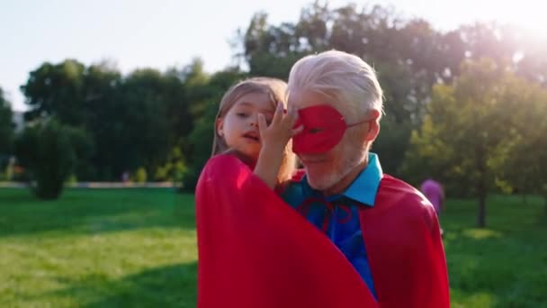 공원 한 복판에서 슈퍼 히어로 옷을 입고 카메라 앞에 포즈를 취하고 있는 행복 한 할아버지와 귀여운 조카 — 비디오