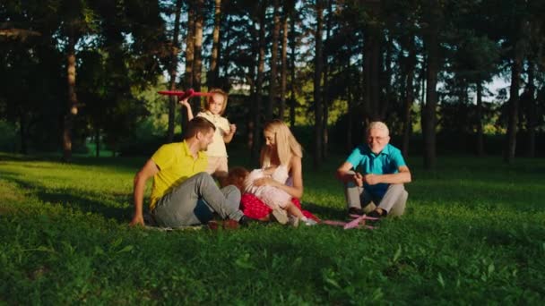 Eine große Familie mit zwei süßen Kindern und ihrem Großvater, die glücklich in der Mitte des Parks spielen, alle zusammen laufen und den Moment genießen — Stockvideo