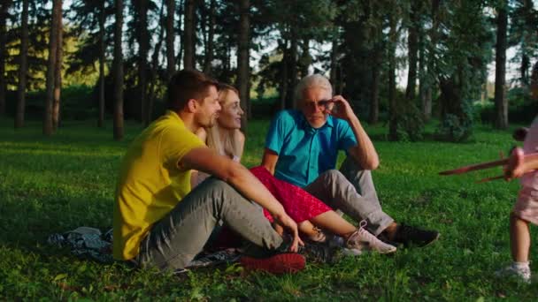 Davanti alla macchina fotografica felice e carismatica bambina carina ei suoi genitori e nonno godono il tempo a contatto con la natura mentre giocano con la bambina — Video Stock