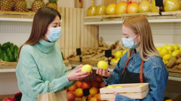 Karizmatikus eladónő védő maszkkal, aki friss citrommal tart egy ládát, és esélyt ad arra, hogy válasszon az ügyfél hölgy számára a koronavírus világjárványban. 4k — Stock videók