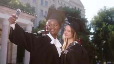 Mezuniyet gününde çok güzel kadınlar üniversite bahçesinde ellerinde diplomalarla selfie çekiyorlar.