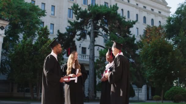 Charismatisch mit einem breiten Lächeln unterhalten sich die Absolventen Damen und Herren nach dem Abschluss mit ihren Diplomen — Stockvideo