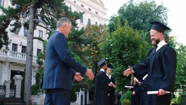 Alter Mann gratulierte seinem Sohn zum Schulabschluss, der junge Mann mit der Mütze schüttelte seinem Vater aufgeregt die Hand, als er das Diplom in der Hand hielt — Stockvideo