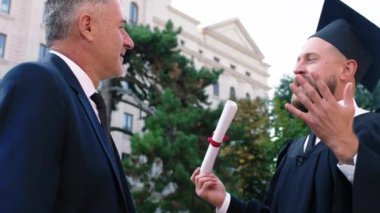 Yakışıklı adam mezuniyetten sonra babasıyla konuşmuş. Mezun olduktan sonra üniversite bahçesinde tartıştıkları diplomasını tutuyor.