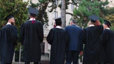 Mezuniyetten sonra birlikte üniversite profesörüyle birlikte üniversite parkına yürüyüp arka plandan video çekmeyi tartışan bir grup çok ırklı öğrenci.