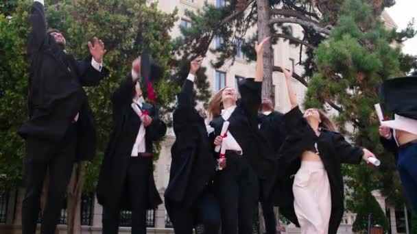 No dia do sol no jardim da faculdade grupo multirracial de jovens estudantes graduados na frente da câmera vomitar as tampas de formatura e sorrindo grande. Tiro em ARRI Alexa Mini. — Vídeo de Stock