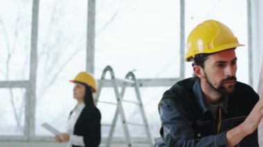 Modern inşaat alanı kameranın önünde iyi görünümlü inşaat işçisi duvarı analiz ederken denetçi kadın dijital tabletle bazı fotoğraflar çekiyor ve sonra adama göstermek için geliyor.