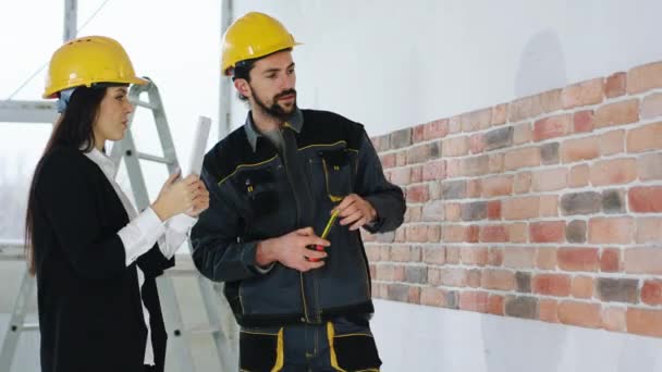 Auf der Baustelle unterhält sich die schöne Supervisorin im schwarzen Anzug mit dem Bauarbeiter, sie misst und fotografiert mit dem digitalen Tablet. — Stockvideo