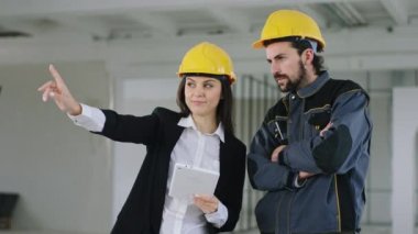 İnşaat işçisi ve kadın mühendis kameranın önünde iş planlarını analiz ederken bir yerde yoğunlaşmışlar.