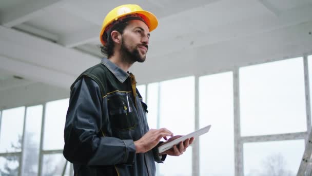 Homem trabalhador construtor feliz segurando tablet digital para analisar algum trabalho no local de construção ele vestindo uniforme especial e capacete amarelo de segurança — Vídeo de Stock