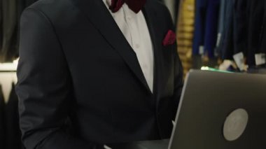 Küçük işletme atölyesi fikri tasarımcı Afro-Amerikan görünümlü adamın yeni takım elbise koleksiyonunun satışlarını kontrol etmek için dizüstü bilgisayarı kullanmasına uyuyor.