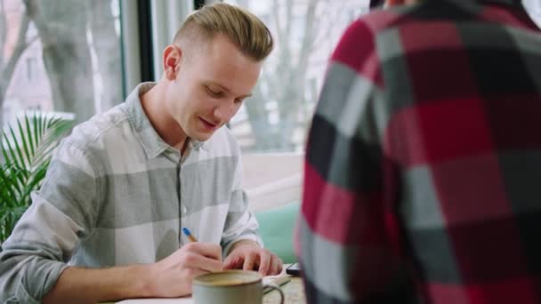 V kavárně dva studenti spolu dělají vysokoškolský projekt. Jeden z nich něco napsal a druhý použil notebook. — Stock video