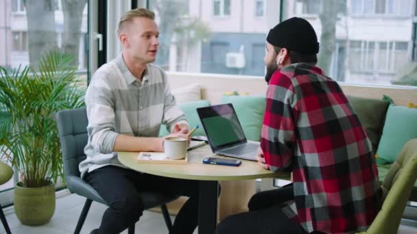 В современной кофейне два хороших друга ребята обсуждают за кофе улыбаясь большой и наслаждаться моментом вместе — стоковое видео