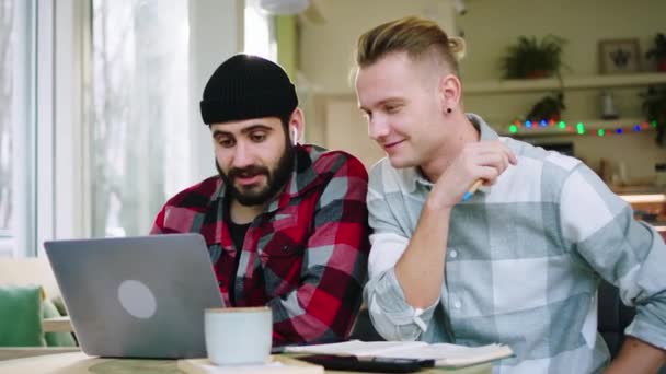 Улыбаясь большой харизматичный два молодых человека студенты у них есть проект колледжа, чтобы сделать вместе с помощью ноутбука, чтобы сделать некоторые заметки в кафе — стоковое видео