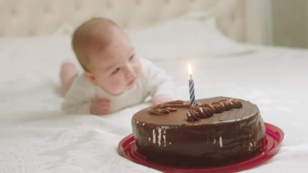 V ložnici před kamerou holčička leží na posteli, zatímco čokoládový dort se svíčkou jsou před ní — Stock video