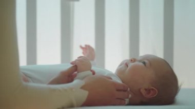 Güzel, tatlı bir kız bebek kızının ellerine dokunarak ve bebek beşiğindeyken dikkatlice oynayarak anne ile hız yapıyor.