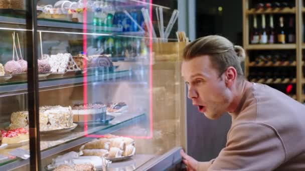 現代のコーヒーショップで興奮した男の顧客非常にカリスマショーケースからいくつかの新鮮でおいしいデザートを選択冷蔵庫 — ストック動画