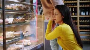 Kahve dükkanındaki güzel bir çift buzdolabına bakıyor. Kadın, erkeğine hangi tatlıyı bulduğunu göstermekten heyecan duyuyor.