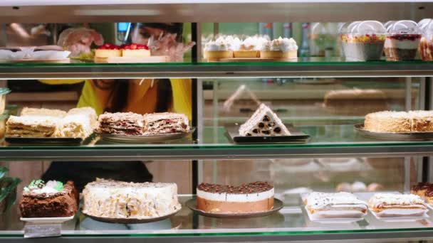 В современной пекарне-кафе продавщица, работающая осторожно, аккуратно расставляет витрину холодильника и надевает защитную маску в пандемии коронавируса — стоковое видео