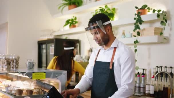 En la cafetería, un guapo barista afroamericano posando frente a la cámara mientras usa máscaras protectoras en la pandemia del coronavirus. — Vídeo de stock