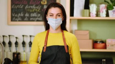 Küçük işletme ve girişimci kavramı kahve dükkanının sahibi kameranın önünde poz veriyor koruyucu maskesini çıkarıyor ve büyük bir salgın halinde gülümsüyor.