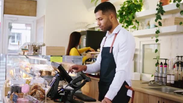 Charismatic Afro American guy in the coffee shop typing a order on the terminal then looking to the camera and smiling large. 4k — Stock Video