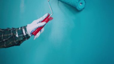 Yakın plan çekimde duvarları mavi renkte boyayan adam duvar fırçası silindirini kullanarak yakın plan video çekiyor.