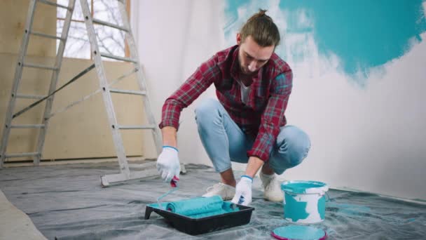 Харизматичный человек сконцентрирован с помощью контейнера, наполненного синим цветом возьмите настенный ролик кисти, чтобы взять некоторый цвет, чтобы начать картину стены — стоковое видео