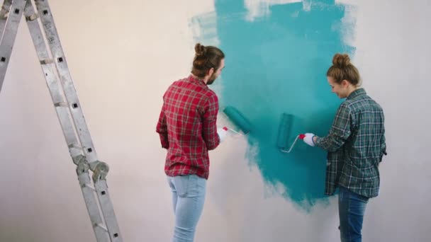 白人カップル非常にカリスマ絵画は、青い色のリビングルームの壁に彼らは壁のブラシローラーでいくつかの楽しみを持っています — ストック動画