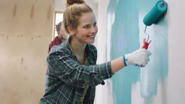 Dans une chambre ensoleillée couple jeune regardant ensemble les murs de peinture à la maison heureux en utilisant le rouleau de brosse murale dame souriant grand. 4k — Video