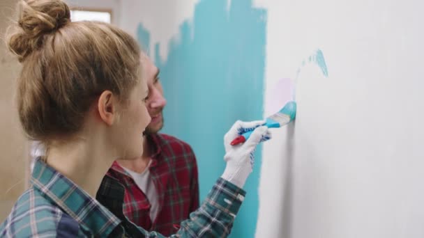 Tomando video primer plano de una hermosa pareja joven caucásica buscando pintar juntos un gran hart en la pared de su sala de estar disfrutan del momento en casa — Vídeo de stock