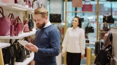 Modern bir aksesuar dükkanında güzel bir satıcı dijital tablet kullanarak fiyatlarda değişiklik yaparken diğer müşteri kadın mağazaya girip bir çanta bulmaya çalışıyor. ARRI Alexa Mini 'de çekilen.