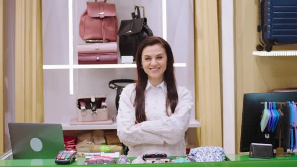Toll aussehende Verkäuferin, die am Terminal-Schreibtisch steht und mit verschränkten Händen vor der Kamera posiert und süß lächelt — Stockvideo