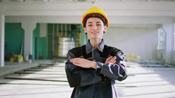 Концепція молодих будівельників, які позують перед камерою на будівельному майданчику, молода жінка з шоломом безпеки та обладнанням вона перетинає руки і дивиться прямо на камеру — стокове відео