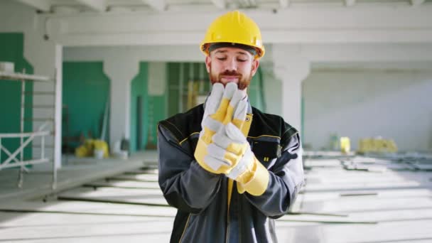 İnşaattaki büyük, aydınlık bir binada çekici bir inşaat işçisi koruyucu eldivenlerini giyiyor ve kameranın önünde güvenlik kaskı ve üniforması ile gülümsüyor. 4k — Stok video
