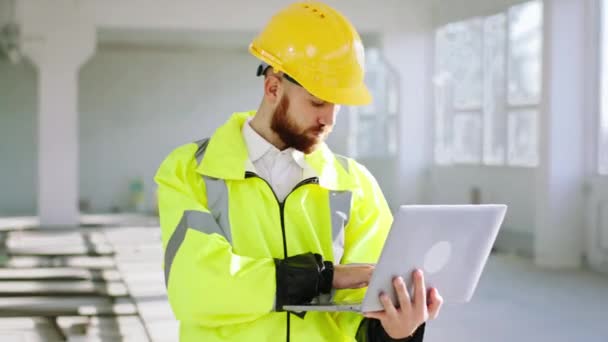 Charismatický inženýr na staveništi ve speciální uniformě držící notebook a pracující soustředěný na stavební plán. 4k — Stock video