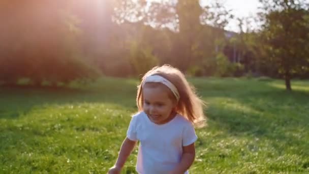 Söt liten flicka som springer genom gräset i mitten av parken hon är glad och upphetsad över naturen — Stockvideo