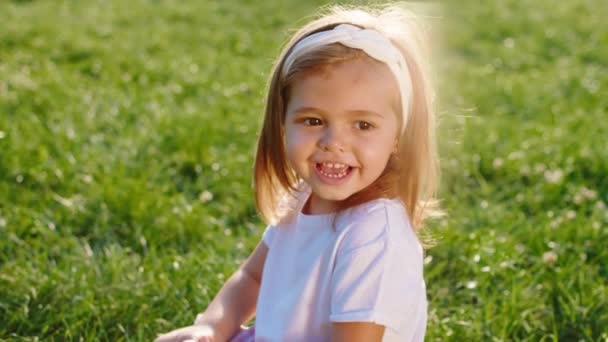 Em um dia de verão perfeito bela menina closeup para a câmera posando enquanto se senta na grama, em seguida, levante-se e começar a correr. 4k — Vídeo de Stock