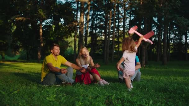 Glückliche Familienzeit im Park niedliches kleines Mädchen und ihre Eltern zusammen mit Opa spielen mit einem großen rosa Flugzeug und lächeln großes Gefühl groß — Stockvideo