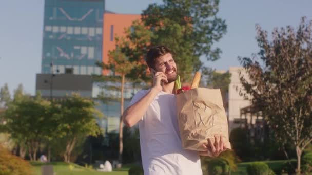 En una ciudad moderna caminando por el hombre de la calle con una bolsa ecológica llena de comida habla por teléfono y sonriendo a lo grande volvió después de la tienda. Arri Alexa Mini. — Vídeo de stock