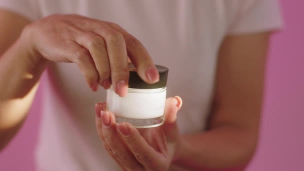 Na różowym tle kobieta otworzyć krem nawilżający i za pomocą palca podjąć pewne pojęcie produktu zdrowej skóry kosmetyki leczenie — Wideo stockowe