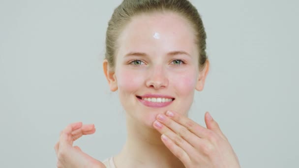 Sur fond blanc belle dame à la peau parfaite faire masser son visage après avoir appliqué un peu de crème hydratante soin sur le visage concept de cosmétiques de traitement de la peau saine. 4k — Video