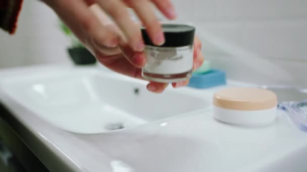 Mengambil rincian seorang wanita membuka krim pelembab favoritnya di kamar mandi dia merawat kulit dan wajahnya — Stok Video