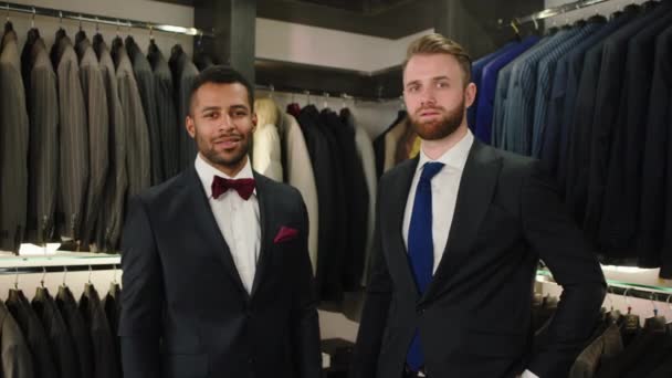 Voor de camera Afro Amerikaanse man en een charismatische blanke man poseren in het pak voor de camera ze zijn in de luxe pak winkel — Stockvideo