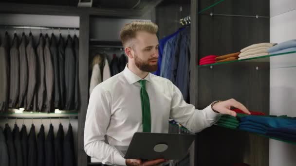 In de luxe pak winkel consulent man Kaukasisch op zoek check de voorraad kleding en pakken uit de winkel — Stockvideo