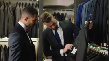 Harika görünümlü Afro-Amerikan damat düğün için en iyi takımı seçmeye çalışıyor. Danışman en iyi kararları vermek ve daha çok takım elbise göstermek için yardım etmeye çalışıyor.