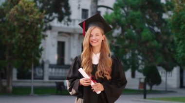 Kolej bahçesinde diplomasını tutarken kameranın önünde poz veren gülümseyen güzel bir bayan. ARRI Alexa Mini 'de çekilen.