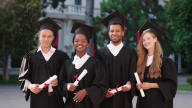 Çok kültürlü mezunlardan oluşan mutlu ve heyecanlı bir grup. Kameraların önünde diplomalarıyla poz veriyorlar.