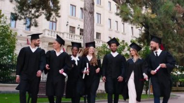 Güneşli bir günde kolej bahçesinde karizmatik çekici öğrencilerden oluşan bir grup mezuniyetten sonra hep birlikte kameranın önünde yürüyorlar ve gülümsüyorlar.